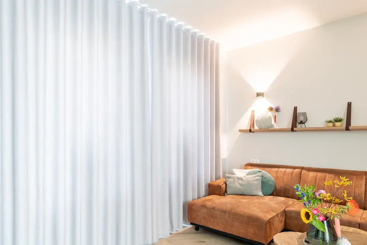 Een wand lichte overgordijnen, dicht, met licht boven de rail